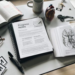 K&ouml;nnte beinhalten: Ein Flatlay-Bild eines wei&szlig;en Tisches mit einem schwarz-wei&szlig;en Spiralblock mit dem Text "Progress Notes" auf dem Cover. Der Block ist auf einer Seite mit den &Uuml;berschriften "The Concept", "The Contributors" und "The Readers" ge&ouml;ffnet. Auf dem Tisch liegen au&szlig;erdem zwei schwarze Stifte, eine Brille, eine Bibel, ein Modell eines menschlichen Herzens, eine Pinzette, eine Schere und ein Buch mit einem Diagramm eines Gehirns.