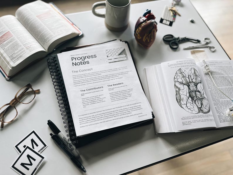 K&ouml;nnte beinhalten: Ein Flatlay-Bild eines wei&szlig;en Tisches mit einem schwarz-wei&szlig;en Spiralblock mit dem Text "Progress Notes" auf dem Cover. Der Block ist auf einer Seite mit den &Uuml;berschriften "The Concept", "The Contributors" und "The Readers" ge&ouml;ffnet. Auf dem Tisch liegen au&szlig;erdem zwei schwarze Stifte, eine Brille, eine Bibel, ein Modell eines menschlichen Herzens, eine Pinzette, eine Schere und ein Buch mit einem Diagramm eines Gehirns.