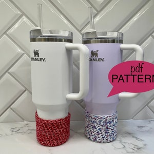 May include: Two Stanley tumblers, one white and one lavender, with white handles and straws. Each tumbler has a crocheted cozy at the base. One cozy is red and white, the other is blue, purple, and white. A pink speech bubble says "pdf PATTERN".