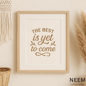 May include: A framed print with the text "THE BEST is yet to come" in brown script. The print is in a light wood frame and has a cream-colored background. The bottom right corner has the text "NEEM DIGITAL DESIGNS".