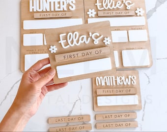 May include: A set of four wooden signs with white lettering and floral accents. Each sign has a blank space for a name and the text "First Day Of". There are also blank spaces for additional information, such as age, height, and things they love. The signs are designed for a first day of school or a first day of something special.