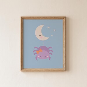May include: A framed wall art print featuring a light purple spider with a small orange bow, hanging from a beige crescent moon with a sleeping face. The background is a solid light blue, and three small white stars are positioned near the moon.