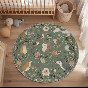 May include: A circular rug with a forest-themed design in shades of green, brown, and peach. The rug features illustrations of hedgehogs, birds, and flowers. It is placed on a wooden floor, near a cot and a wicker basket.