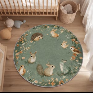May include: A circular rug in sage green, decorated with woodland animals including rabbits, squirrels, and an owl. The rug has a floral border with orange and yellow flowers and green leaves. It is placed on a light wood floor.