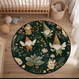 May include: A round, dark green rug featuring whimsical illustrations of gnomes with wings, mushrooms, and floral elements. The rug has a black border and is placed on a wooden floor, with a crib and toys in the background.