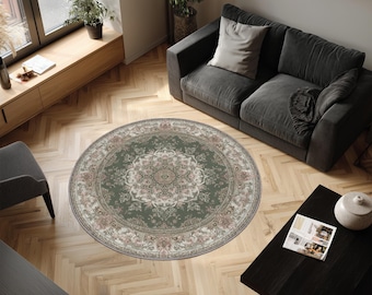 May include: A round, green area rug with an intricate floral pattern in shades of pink, cream, and beige. The rug is centered on a light wood floor, surrounded by furniture, creating a cozy living space.