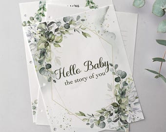 Op de afbeelding: Pagina's van een babyherinneringsboek met de tekst "Hello Baby, the story of you". De pagina's zijn versierd met aquarel eucalyptus en bloemmotieven in groen- en grijstinten, met een gouden geometrisch kader.