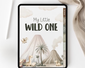 May include: A digital tablet displays a children's book cover with the text "My Little WILD ONE." The illustration features cartoon dinosaurs, volcanoes, palm trees, and clouds in a soft, muted color palette. A stylus rests on the side.