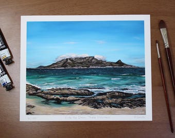 May include: A painting of a mountain range with a cloudy peak, rising from the ocean. The water is a turquoise blue and the sky is a bright blue. The painting is titled "With the Ocean, These Mountains".