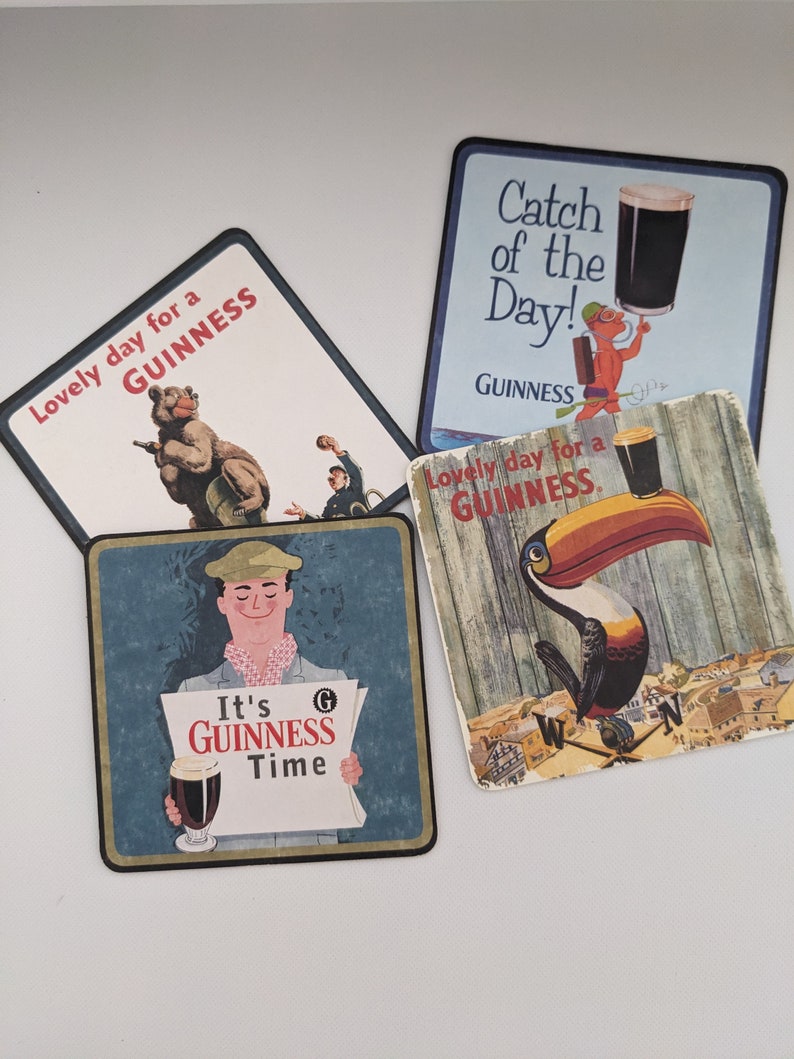 Puede incluir: Cuatro posavasos cuadrados con diferentes ilustraciones y el texto "GUINNESS". Los posavasos son azules, blancos y marrones con im&aacute;genes de un oso, un tuc&aacute;n, un hombre sosteniendo un peri&oacute;dico y un hombre sosteniendo un vaso de cerveza.