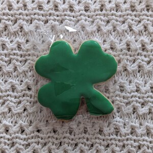 Puede incluir: Una galleta de tr&eacute;bol de cuatro hojas verde en una bolsa de pl&aacute;stico transparente.
