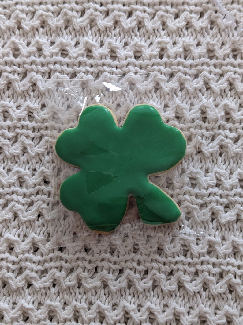 Puede incluir: Una galleta de tr&eacute;bol de cuatro hojas verde en una bolsa de pl&aacute;stico transparente.