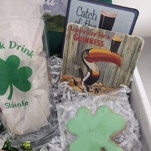Puede incluir: Una caja de regalo de San Patricio con un vaso de tr&eacute;bol verde, una galleta de tr&eacute;bol verde, una barra de chocolate, un posavasos de madera y un posavasos de Guinness con un tuc&aacute;n.