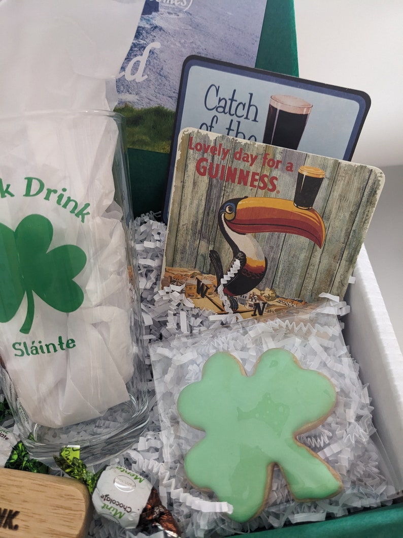 Puede incluir: Una caja de regalo de San Patricio con un vaso de tr&eacute;bol verde, una galleta de tr&eacute;bol verde, una barra de chocolate, un posavasos de madera y un posavasos de Guinness con un tuc&aacute;n.