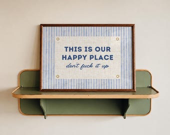 May include: A rectangular framed print with a light blue and white vertical striped background. The center features a white rectangular panel with the text "THIS IS OUR HAPPY PLACE" in blue block letters and "don't fuck it up" in blue script.