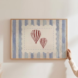 May include: Framed artwork featuring two red and white hot air balloons on a cream background. The background has a blue and white striped pattern. The artwork is in a wooden frame.