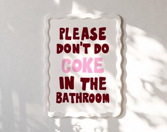 May include: A white, rectangular sign with a wavy border. The sign features the text "PLEASE DON'T DO COKE IN THE BATHROOM" in maroon and pink lettering. The sign is mounted on a white wall.