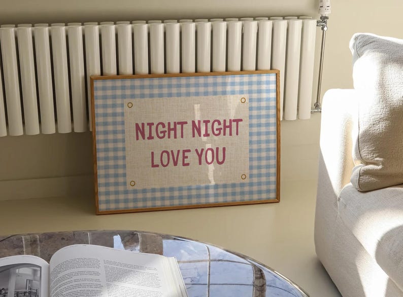 May include: A framed wall art piece with a light blue and white gingham pattern border. The center features a linen-colored rectangle with the words "NIGHT NIGHT LOVE YOU" in pink lettering. The frame is a light brown color.