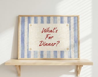 May include: A framed sign with the text "What's For Dinner?" in red script. The background features blue and white vertical stripes, with a beige rectangular area in the center. The frame is made of light-colored wood.
