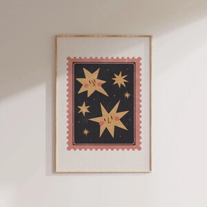 May include: A framed print with a pink and black border featuring a whimsical illustration of five gold stars with smiling faces against a dark blue background.