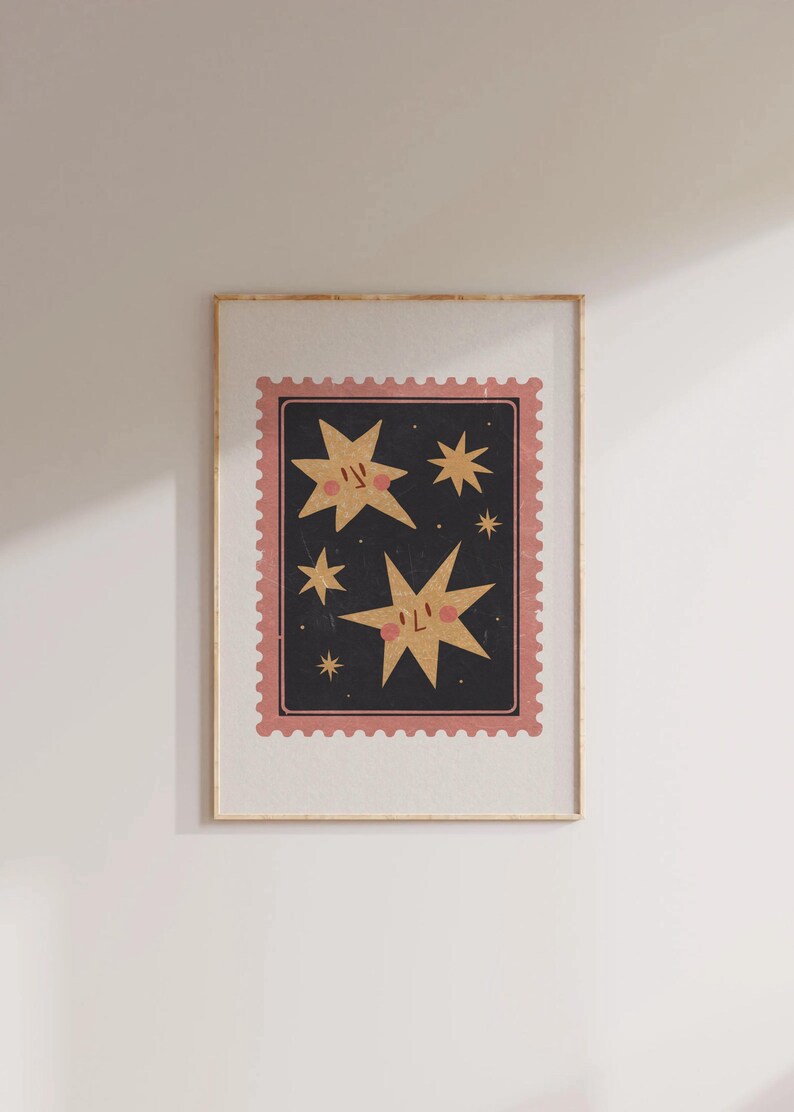 May include: A framed print with a pink and black border featuring a whimsical illustration of five gold stars with smiling faces against a dark blue background.