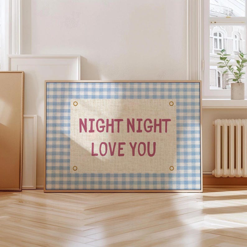 May include: A framed artwork with a light blue and white gingham pattern background. The artwork features a beige rectangle with the words "NIGHT NIGHT LOVE YOU" in pink lettering. The frame is a light wood color.