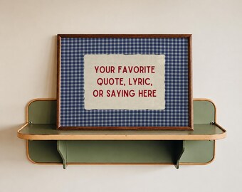 May include: A rectangular framed print featuring a blue and white gingham pattern background with a central cream-colored paper cutout containing the red text: YOUR FAVORITE QUOTE, LYRIC, OR SAYING HERE. The frame is dark brown wood.