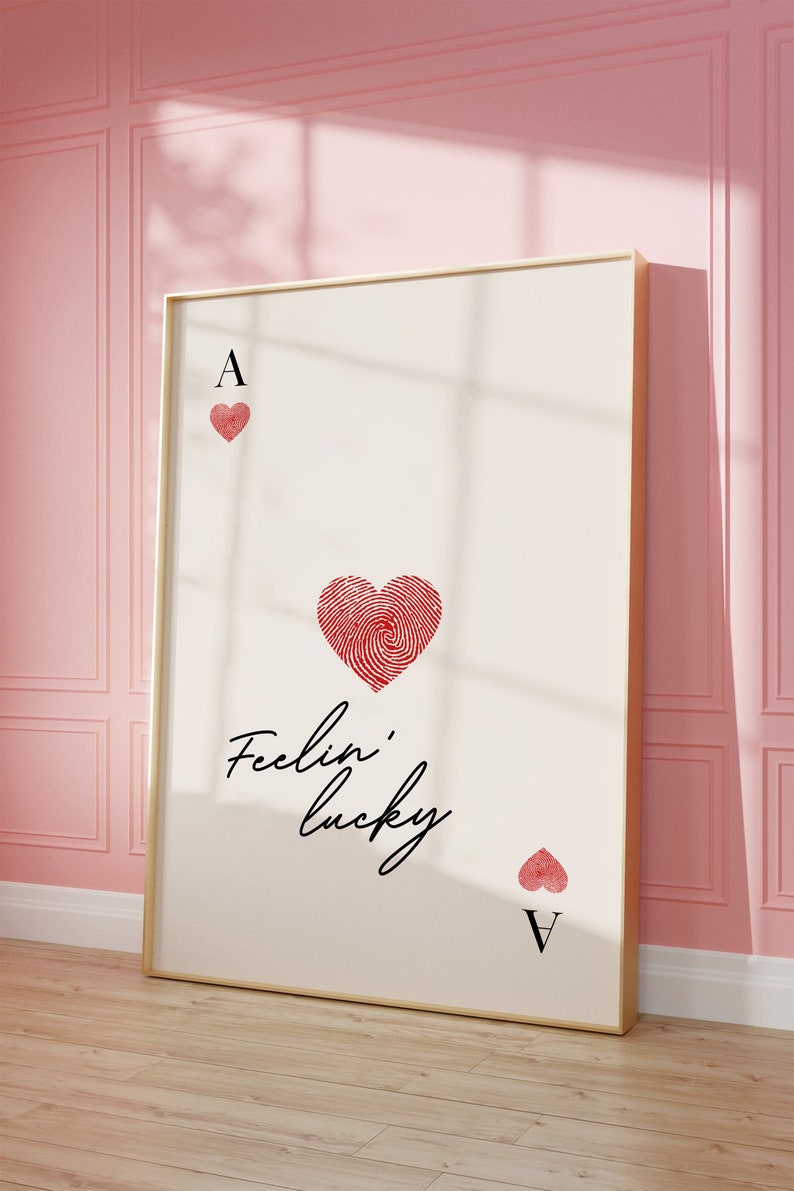 Op de afbeelding: Een ingelijst afdruk van een aas harten speelkaart met een vingerafdruk ontwerp in de vorm van een hart. De tekst "Feelin' lucky" is in cursief geschreven onder het hart.