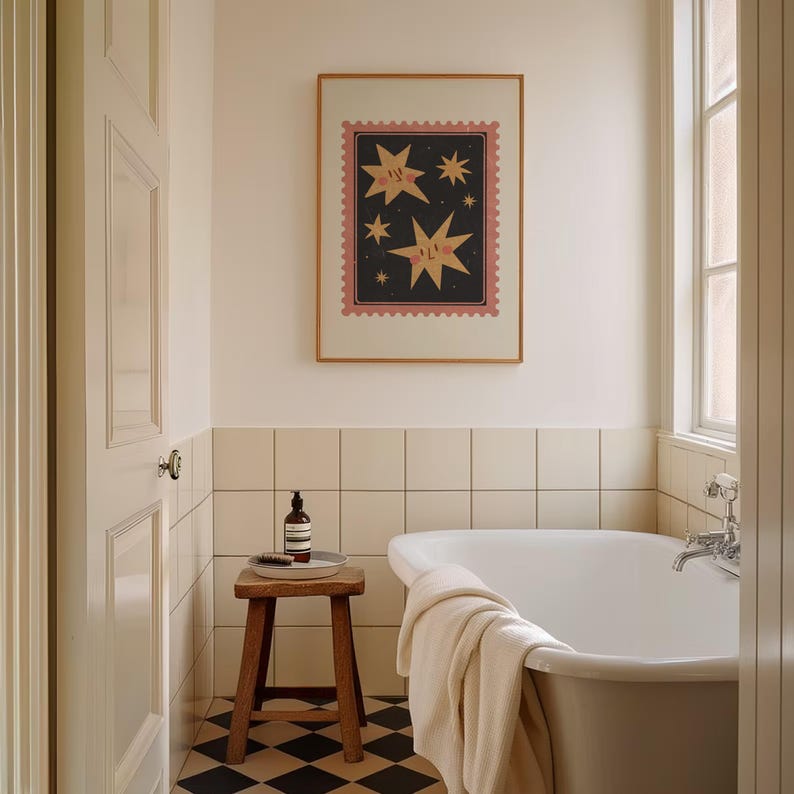 May include: A white bathtub with a towel on the side, a wooden stool with a bottle of soap on it, and a framed print of stars with faces on a black background in a white bathroom with white tile.