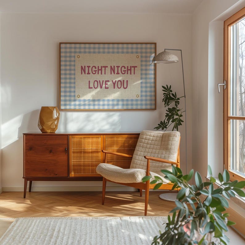 May include: A mid-century modern living room with a wooden cabinet, a beige armchair, and a framed artwork that reads "NIGHT NIGHT LOVE YOU". A gold vase sits on the cabinet. A floor lamp and a houseplant are also visible.