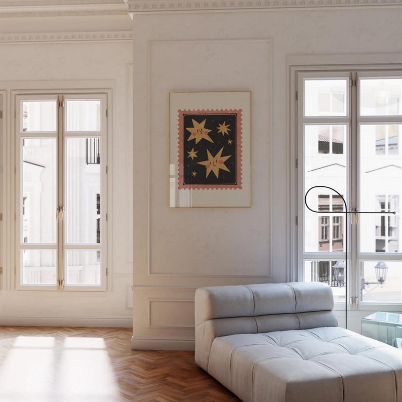 May include: A white couch with a black metal floor lamp in a room with white walls and large windows. A framed print with a pink and black design hangs on the wall. The print features a black background with pink stars and the words "You're a Star".