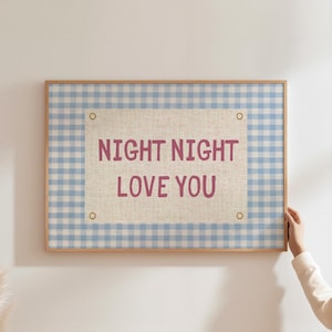 May include: A framed wall art piece with a light blue and white gingham pattern border. The center features a beige canvas with the words "NIGHT NIGHT LOVE YOU" in a mauve color. The frame is a light brown color.