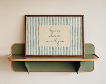 May include: A rectangular wooden frame containing a print with vertical sage green and white stripes. Centered on the print is a cream-colored rectangular insert featuring the dark green text, "home is wherever i'm with you" in cursive.