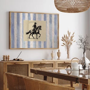 Pu&ograve; includere: Una stampa incorniciata di un'illustrazione in bianco e nero di un cowboy a cavallo. La stampa &egrave; su uno sfondo di strisce blu e bianche. La stampa &egrave; appesa a un muro bianco sopra un armadio in legno.