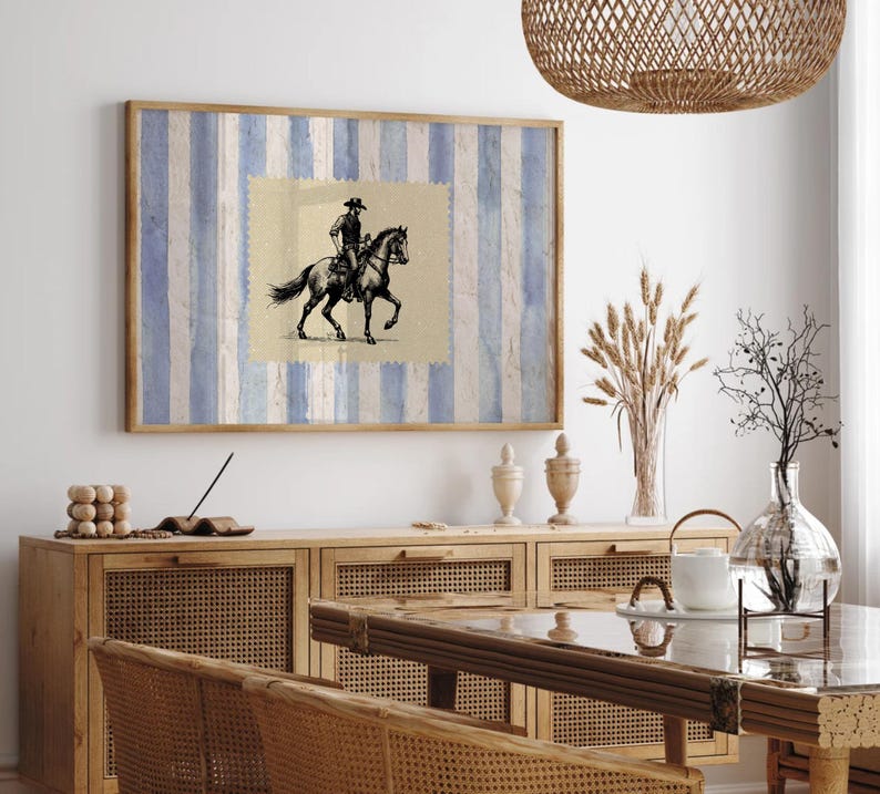 Pu&ograve; includere: Una stampa incorniciata di un'illustrazione in bianco e nero di un cowboy a cavallo. La stampa &egrave; su uno sfondo di strisce blu e bianche. La stampa &egrave; appesa a un muro bianco sopra un armadio in legno.