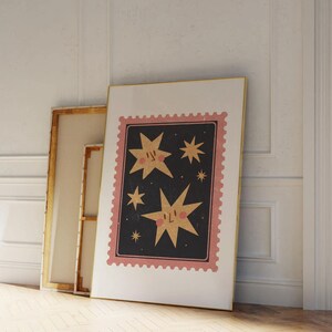 May include: A framed print with a pink and white border featuring a black background with gold stars. The stars have faces and blush on their cheeks.