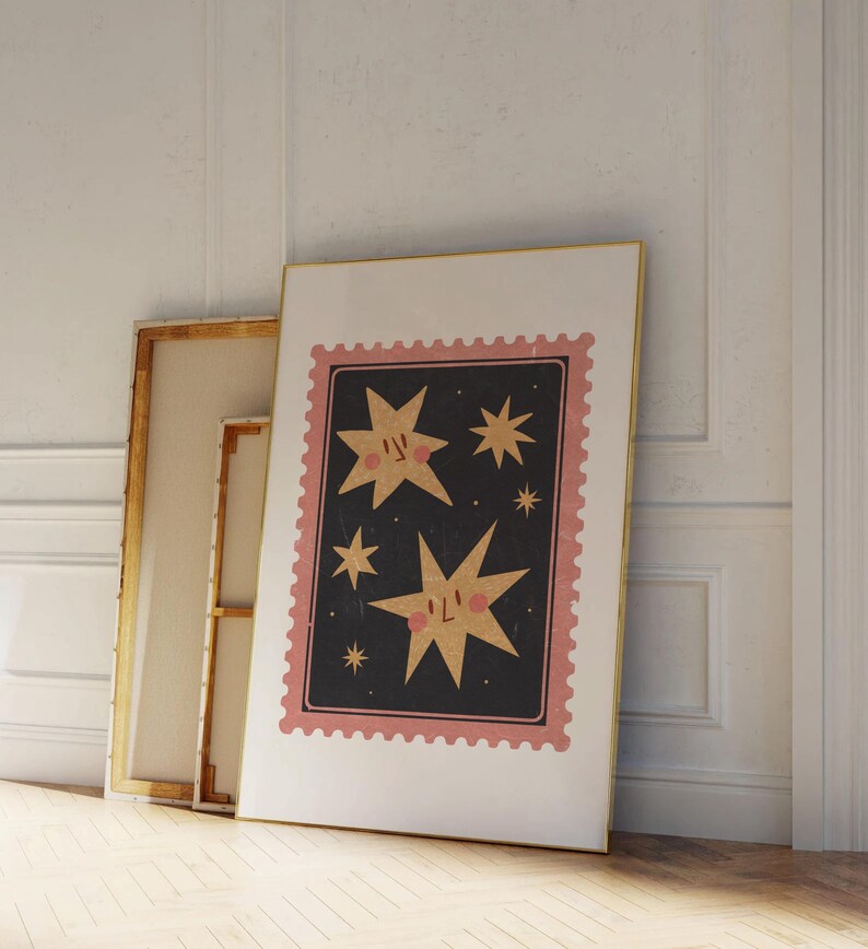 May include: A framed print with a pink and white border featuring a black background with gold stars. The stars have faces and blush on their cheeks.