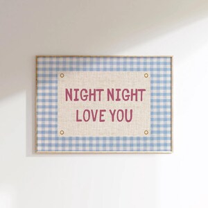May include: A framed wall art piece with a light blue and white gingham pattern border. The center features a beige fabric with the words "NIGHT NIGHT LOVE YOU" in a dark pink font. The frame has a light wood finish.
