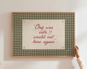 May include: A framed wall art piece with a plaid green and brown border. The center features a beige canvas with the quote "Chef was cute, would eat here again" in red script.