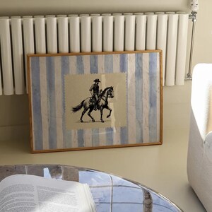 Pu&ograve; includere: Una stampa incorniciata di un'illustrazione in bianco e nero di un cowboy a cavallo. La stampa &egrave; su uno sfondo a strisce blu e bianche.