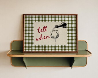 May include: A rectangular framed print featuring a green and white gingham border. The center shows a black and white illustration of wine pouring from a bottle into a glass, with the red cursive text tell when written to the left side.