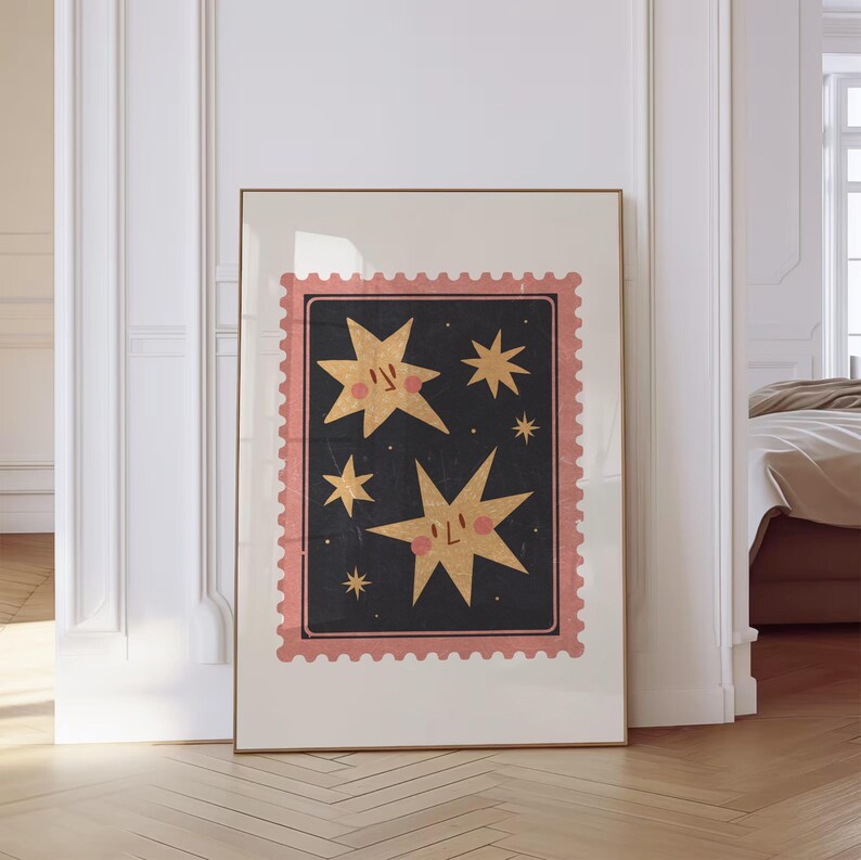 May include: A framed print with a pink and black design featuring two gold stars with faces and smaller stars. The print has a vintage postage stamp look.