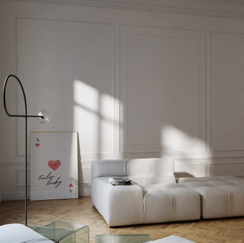 Op de afbeelding: Een witte modulaire bank met een witte, gestructureerde stof. De bank staat in een kamer met witte muren en een ingelijst afdruk van een harten aas met de tekst "feelin' lucky".