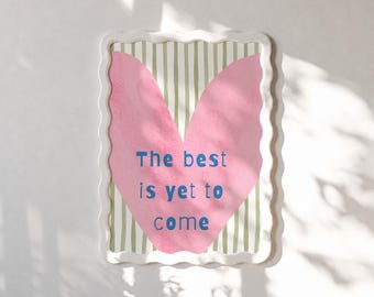 May include: A rectangular wall art piece with a wavy white frame. The print features a large pink heart shape centered over a background of vertical olive green and white stripes. The text "The best is yet to come" is printed in blue.