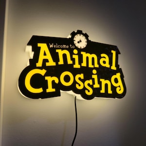 Pu&ograve; includere: Insegna luminosa con la scritta "Welcome to Animal Crossing" in giallo su sfondo nero. L'insegna ha una grafica a orologio e un bordo bianco ed &egrave; collegata a una parete.