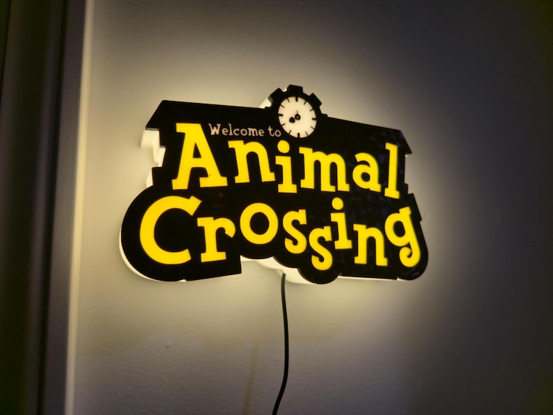 Pu&ograve; includere: Insegna luminosa con la scritta "Welcome to Animal Crossing" in giallo su sfondo nero. L'insegna ha una grafica a orologio e un bordo bianco ed &egrave; collegata a una parete.