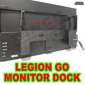 Può includere: Un dock per monitor Legion Go nero con un cavo collegato. Il dock ha diverse porte e una clip. Il testo "LEGION GO MONITOR DOCK" è visualizzato in lettere rosse con un contorno verde. È visibile anche il testo "Monitor and cable are not included".
