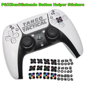 May include: A white and black game controller with the text "TANGO TACTICAL" and button helper stickers. The controller has a black center and white sides. The stickers have colored symbols and letters.