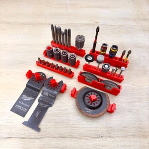May include: A red and black tool organizer with various drill bits, sanding discs, and cutting blades. The organizer has multiple compartments and is labeled "Dremel".