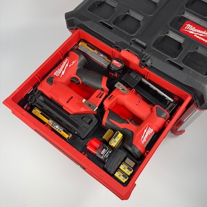 May include: A red and black Milwaukee Packout tool box drawer filled with power tools and accessories. The drawer contains a nail gun, a stapler, batteries, and a tape measure. The tools are neatly organized in the red drawer.